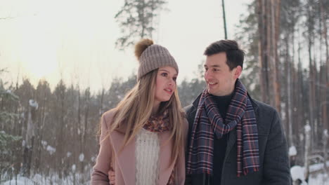 In-the-winter-snowy-forest,-young-men-and-women-dressed-in-coats-and-scarves-are-walking-and-having-fun.-Loving-couple-spend-together-valentines-day.